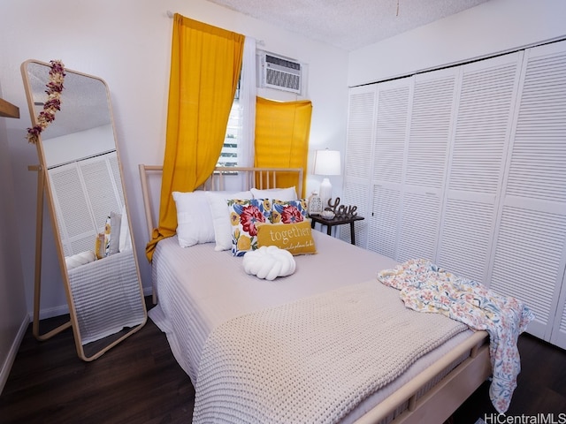 bedroom with a textured ceiling, a closet, a wall mounted air conditioner, and dark hardwood / wood-style flooring