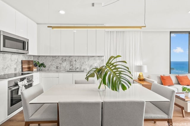 kitchen with a breakfast bar, sink, stainless steel appliances, a water view, and white cabinets