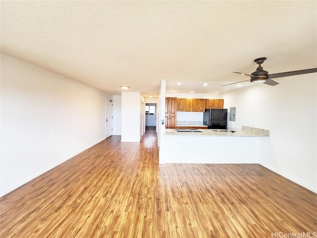 unfurnished living room with a textured ceiling, ceiling fan, light hardwood / wood-style flooring, and electric panel