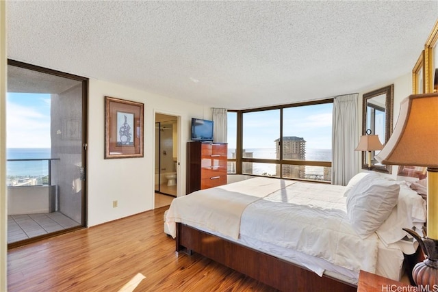 bedroom with a textured ceiling, ensuite bathroom, a water view, and light hardwood / wood-style flooring