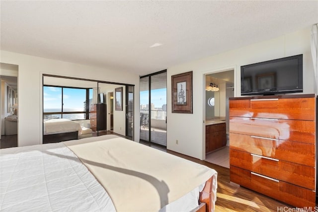 bedroom featuring connected bathroom, light hardwood / wood-style flooring, and a textured ceiling