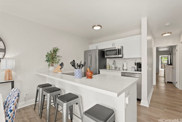 kitchen with a breakfast bar area, appliances with stainless steel finishes, tasteful backsplash, white cabinets, and sink