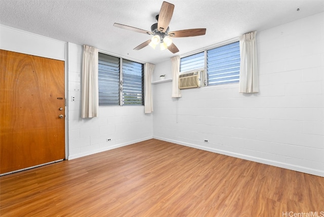 empty room with a textured ceiling, ceiling fan, cooling unit, and wood-type flooring