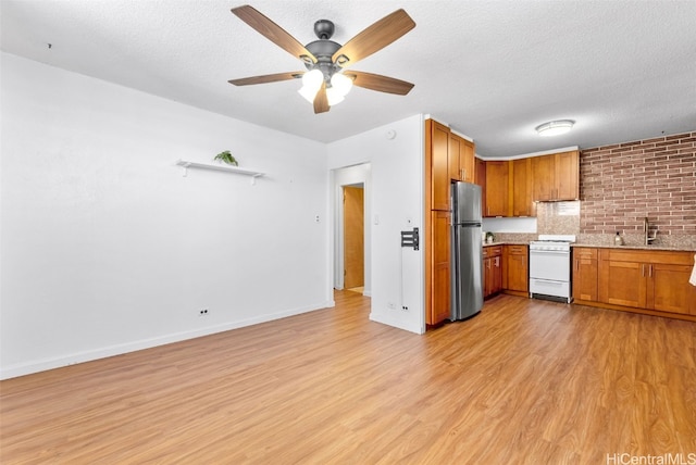 kitchen featuring light wood-type flooring, a textured ceiling, stainless steel fridge, and white gas range oven