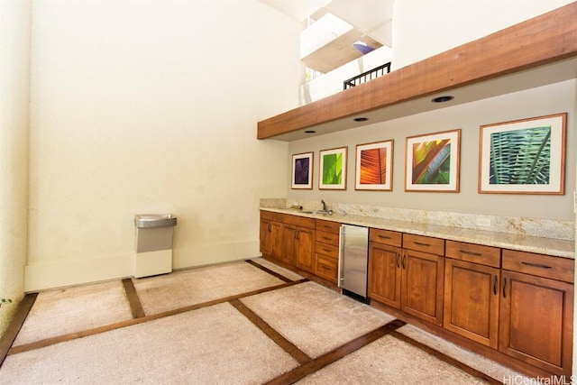 bar featuring light stone counters, a towering ceiling, fridge, and sink