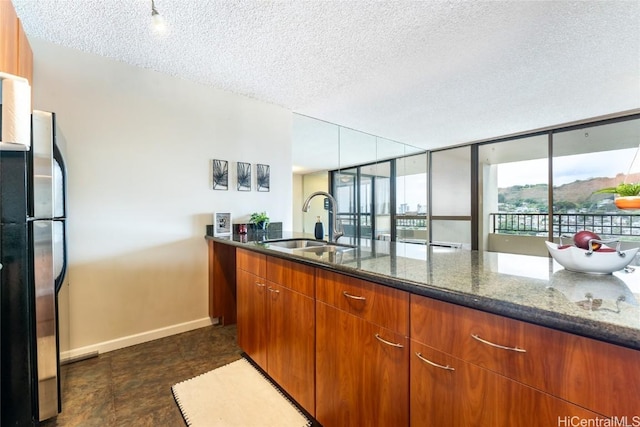 kitchen with sink, a textured ceiling, dark stone counters, and stainless steel fridge