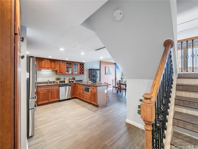 kitchen with vaulted ceiling, light hardwood / wood-style floors, stainless steel appliances, kitchen peninsula, and sink