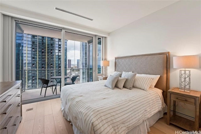 bedroom with light wood-type flooring, access to outside, and a wall of windows