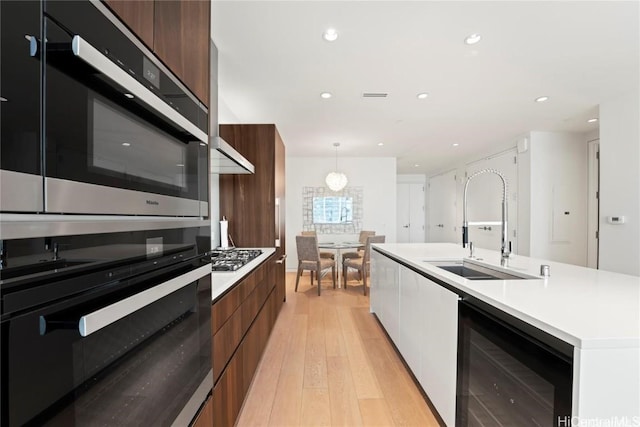 kitchen with decorative light fixtures, an island with sink, wine cooler, light hardwood / wood-style floors, and stainless steel appliances