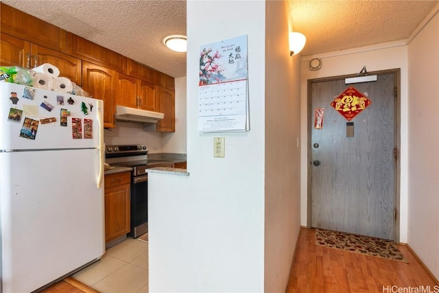 kitchen with white fridge, light wood-type flooring, stainless steel range with electric stovetop, decorative backsplash, and a textured ceiling