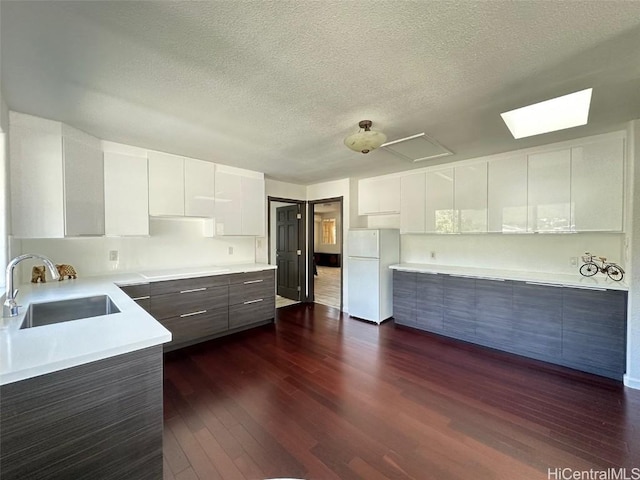 kitchen with a textured ceiling, dark hardwood / wood-style floors, white cabinets, white refrigerator, and sink