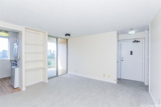 carpeted empty room with a textured ceiling, stacked washer / dryer, and a healthy amount of sunlight