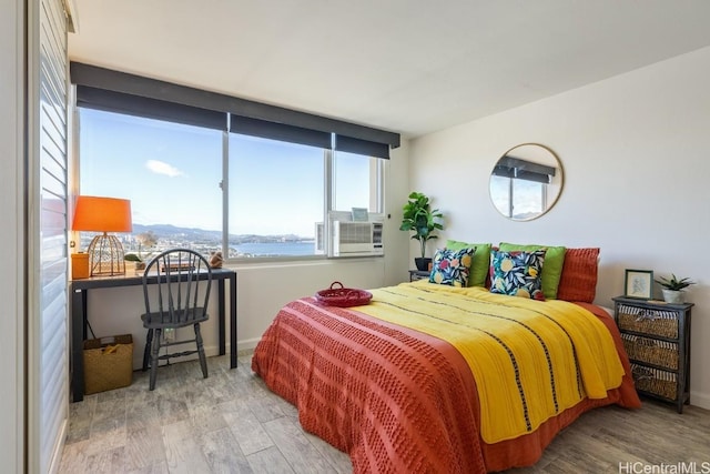 bedroom with hardwood / wood-style flooring, cooling unit, and a water view