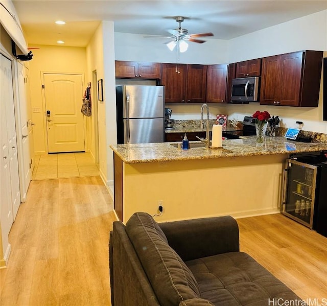 kitchen with sink, stainless steel appliances, beverage cooler, light stone countertops, and light hardwood / wood-style floors