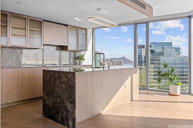 kitchen featuring light hardwood / wood-style floors, stone countertops, black electric stovetop, expansive windows, and sink