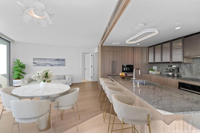 kitchen with sink, black microwave, light hardwood / wood-style floors, a breakfast bar area, and decorative backsplash