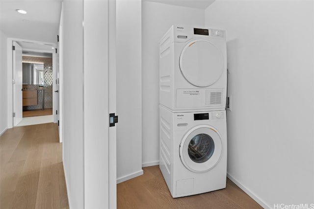 laundry area with light hardwood / wood-style flooring and stacked washer / drying machine