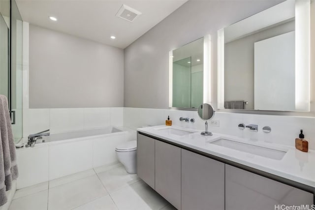 bathroom with toilet, tile patterned flooring, tiled tub, and vanity