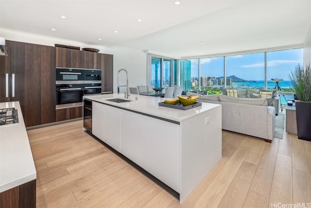 kitchen featuring white cabinetry, light hardwood / wood-style floors, a center island with sink, a wall of windows, and sink