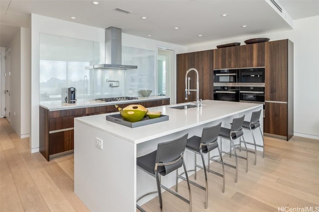 kitchen with a breakfast bar, stainless steel appliances, extractor fan, and an island with sink