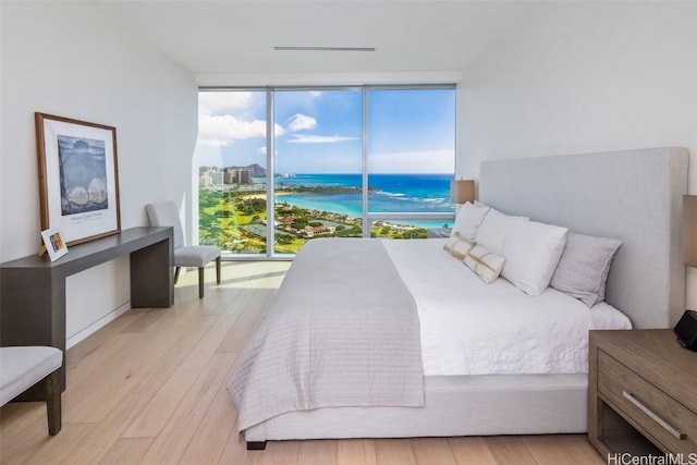 bedroom featuring a wall of windows, a water view, and light hardwood / wood-style floors