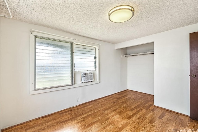 unfurnished bedroom with cooling unit, hardwood / wood-style floors, a closet, and a textured ceiling