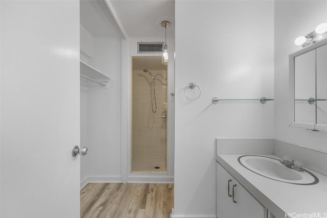 bathroom with vanity, a textured ceiling, hardwood / wood-style flooring, and tiled shower