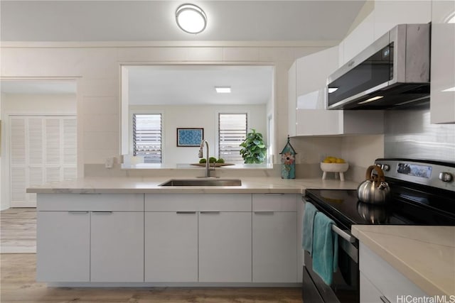 kitchen with sink, white cabinetry, light stone countertops, light hardwood / wood-style floors, and stainless steel appliances