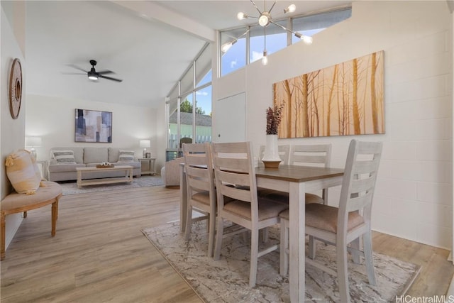 dining space with light wood-type flooring, ceiling fan with notable chandelier, beam ceiling, and high vaulted ceiling