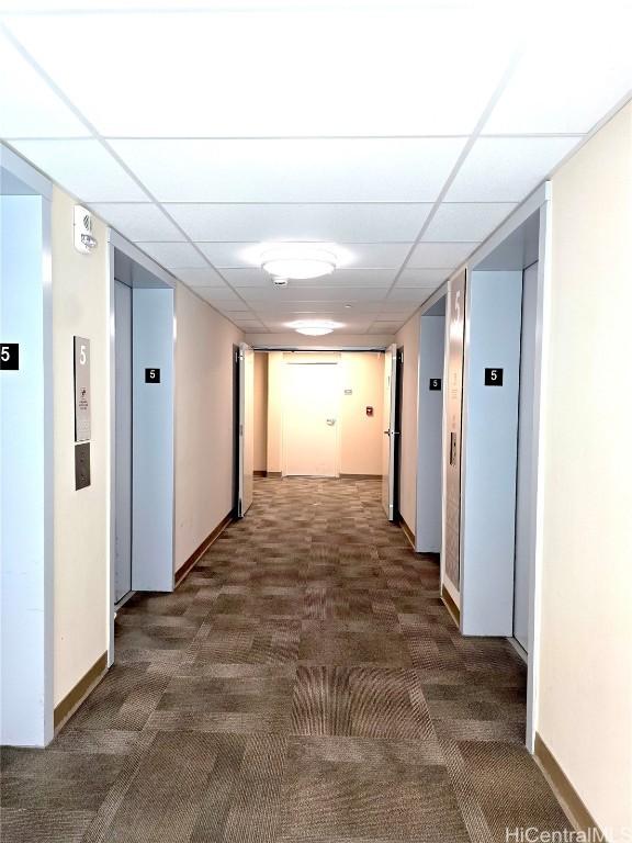 hallway with a paneled ceiling and dark colored carpet