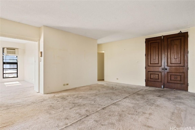 unfurnished room with light carpet, a textured ceiling, and a wall mounted air conditioner