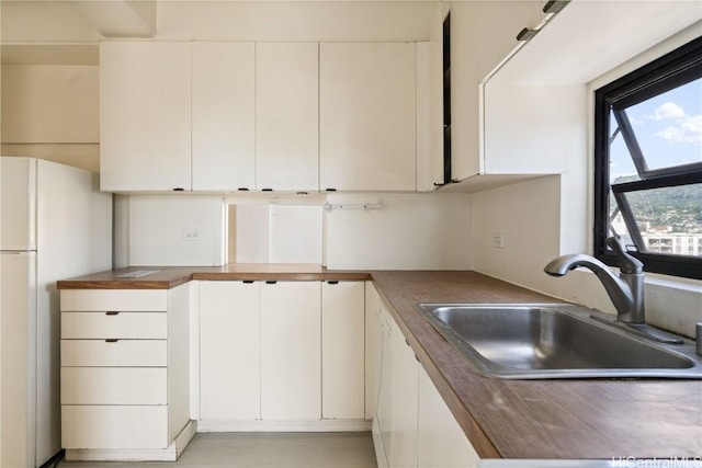 kitchen with white refrigerator, butcher block counters, white cabinets, and sink