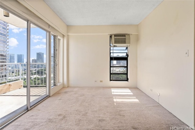 spare room featuring a healthy amount of sunlight, a wall unit AC, a textured ceiling, and carpet flooring