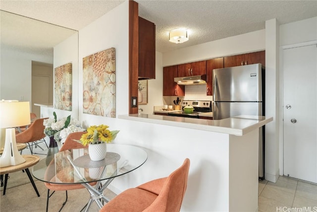 kitchen featuring light tile patterned floors, kitchen peninsula, stainless steel appliances, and a textured ceiling