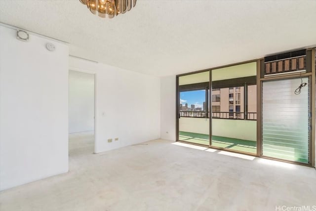 empty room featuring a wall mounted AC, a notable chandelier, floor to ceiling windows, a textured ceiling, and light carpet