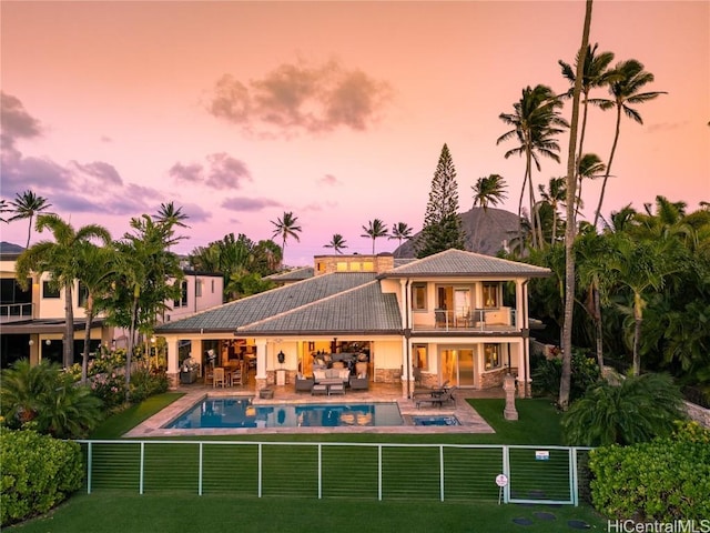 back of property at dusk with a patio, a fenced backyard, a balcony, an outdoor hangout area, and a yard