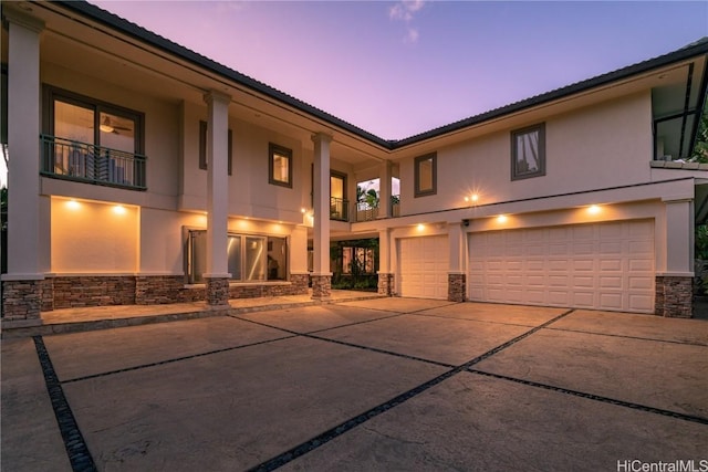 view of front of property featuring a balcony, driveway, an attached garage, stucco siding, and stone siding