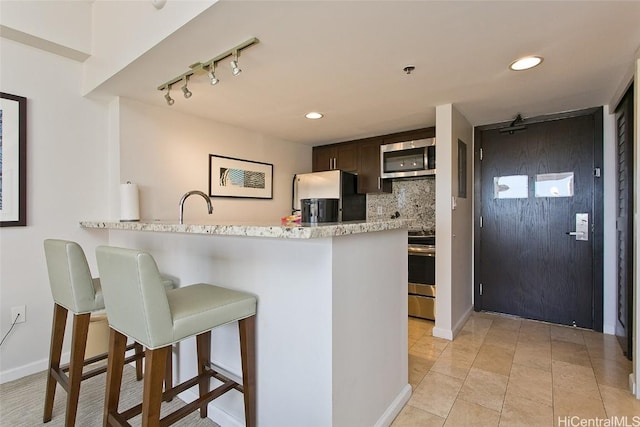 kitchen with decorative backsplash, track lighting, dark brown cabinets, a breakfast bar, and stainless steel appliances