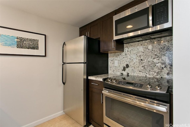 kitchen with stainless steel appliances, tasteful backsplash, light stone counters, light tile patterned floors, and dark brown cabinets