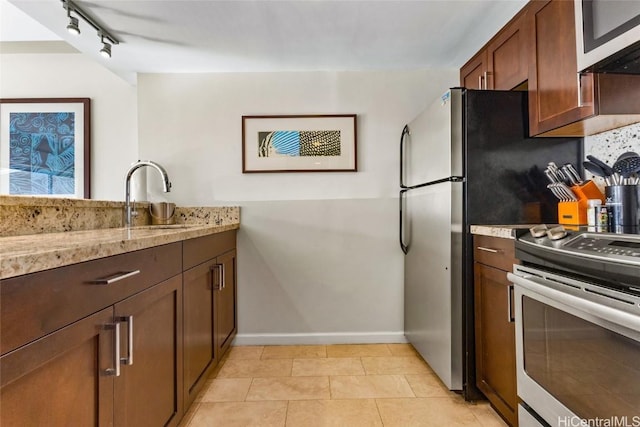 kitchen featuring light stone counters, light tile patterned flooring, stainless steel appliances, a sink, and baseboards