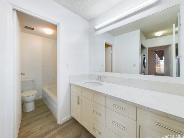 full bathroom featuring a textured ceiling, washer / dryer, wood-type flooring, vanity, and toilet