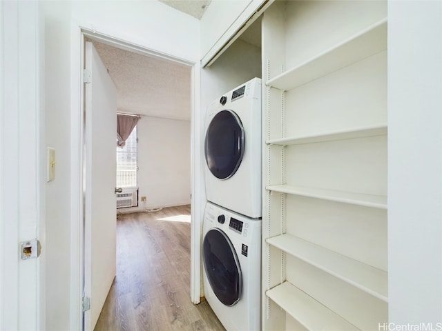 washroom featuring a textured ceiling, stacked washer / drying machine, and light hardwood / wood-style flooring