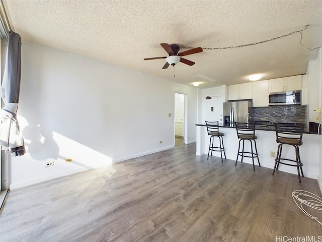 kitchen featuring backsplash, white cabinetry, a kitchen breakfast bar, a textured ceiling, and stainless steel appliances