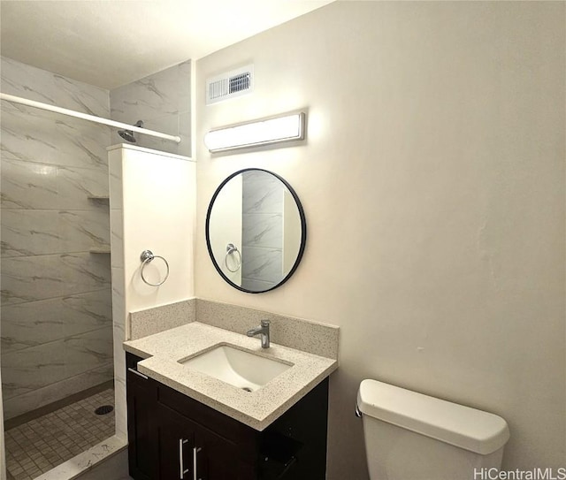 bathroom with toilet, tiled shower, and vanity