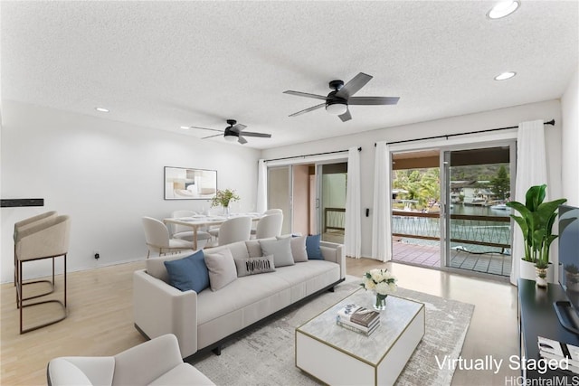 living room with a textured ceiling, ceiling fan, and light hardwood / wood-style floors