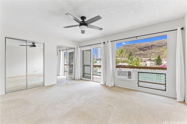 unfurnished bedroom featuring multiple closets, ceiling fan, a textured ceiling, and light colored carpet