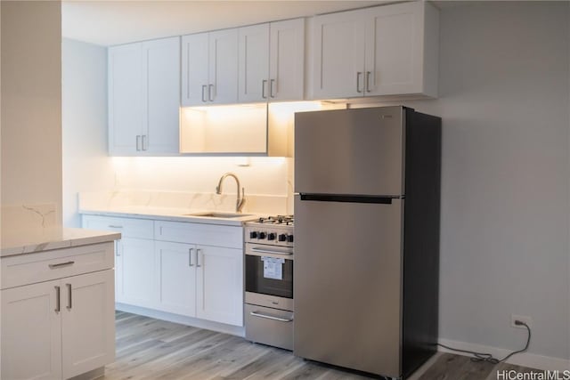 kitchen featuring light stone counters, light hardwood / wood-style flooring, stainless steel appliances, white cabinetry, and sink