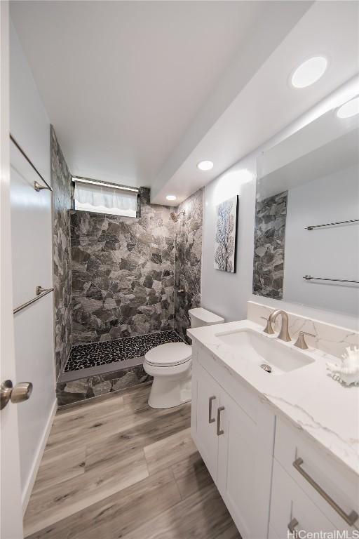 bathroom featuring a tile shower, vanity, toilet, and hardwood / wood-style flooring