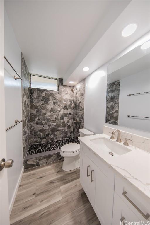 bathroom with toilet, wood-type flooring, tiled shower, and vanity