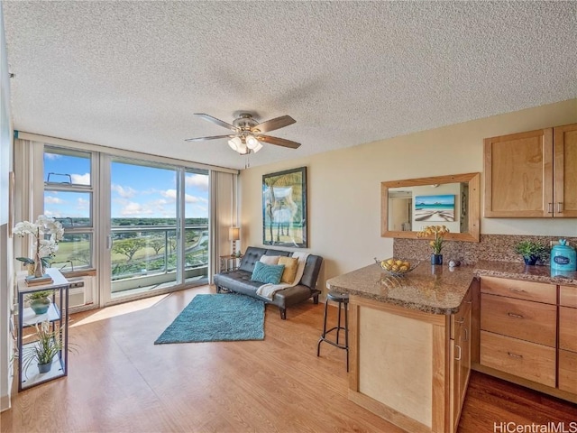 living room featuring ceiling fan, light hardwood / wood-style flooring, floor to ceiling windows, and a textured ceiling